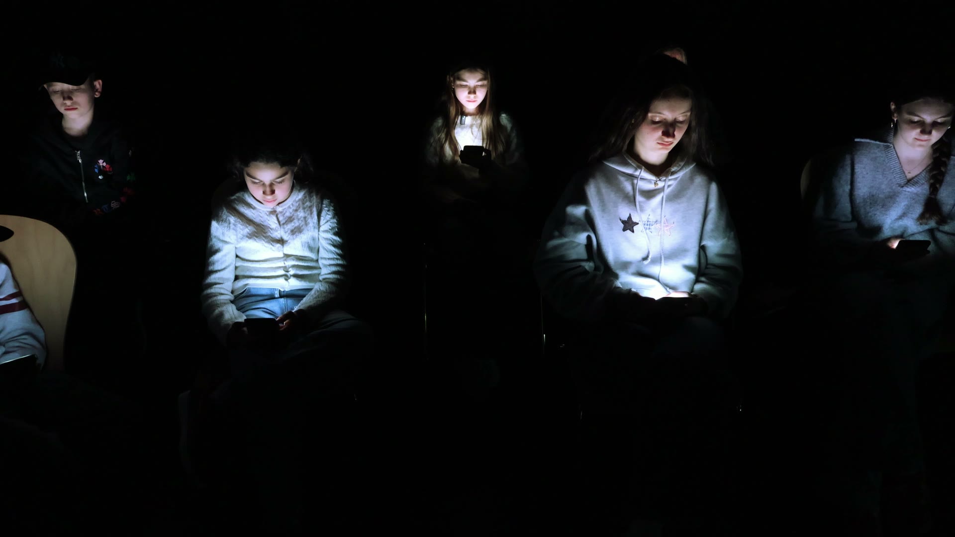 Schülerinnen und Schüler sitzen im Dunkeln, beleuchtet nur vom Licht ihrer Handydisplays